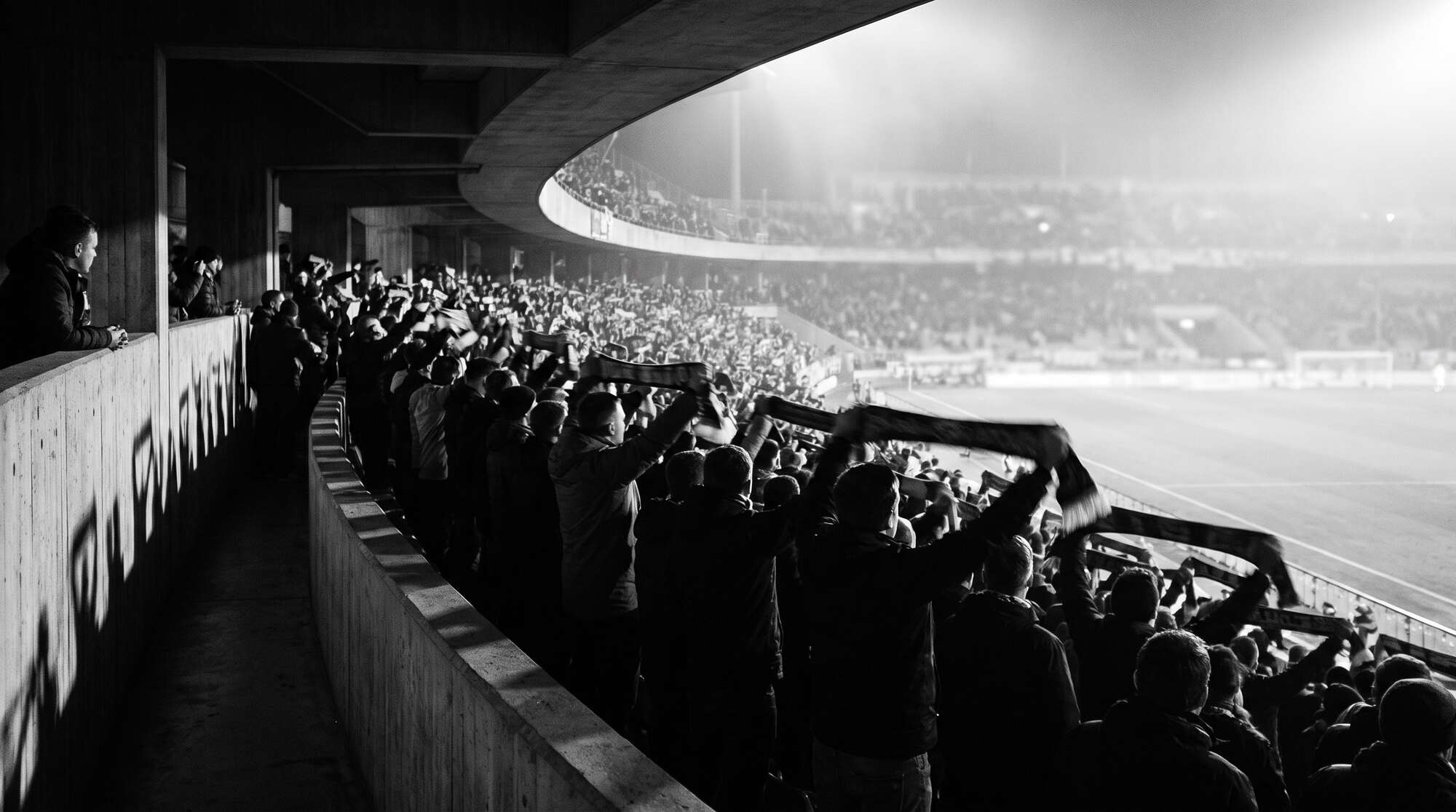 Supporters in the stand shortly before kick-off, scarves in the air, seen from behind